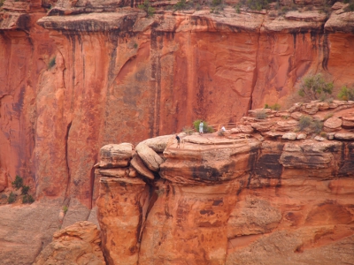 [Several people lean against a railing around one edge of a tall rock wall.]